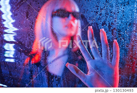 In black sunglasses. Stylish woman with white hair is behind wet transparent plastic sheet 130130493