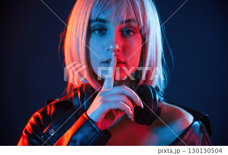 Gesture of be quiet, finger is by the lips. Woman with white hair is in studio with neon colors 130130504