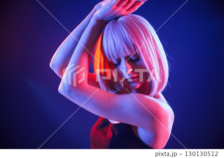 Dancing, with hands up. Woman with white hair is in studio with neon colors 130130512
