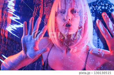 Hands are on the surface. Stylish woman with white hair is behind wet transparent plastic sheet 130130515