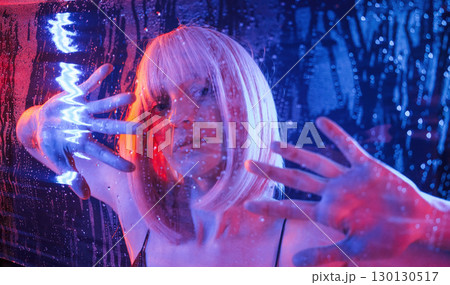 Trapped inside, with hands on surface. Stylish woman with white hair is behind wet transparent plastic sheet Trapped inside, with hands on surface. Stylish woman with white hair is behind wet transparent plastic sheet 130130517