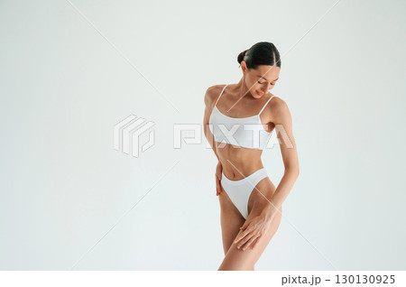 Standing and posing. Woman in white underwear with slim body type against white background 130130925