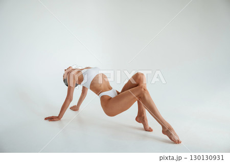 Lying down on the floor. Woman in white underwear with slim body type against white background 130130931
