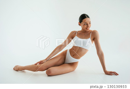 Positive facial expression. Woman in white underwear with slim body type against white background Positive facial expression. Woman in white underwear with slim body type against white background 130130933