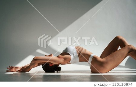 Shadows and sunlight. Doing exercises. Woman in white underwear with slim body type Shadows and sunlight. Doing exercises. Woman in white underwear with slim body type 130130974