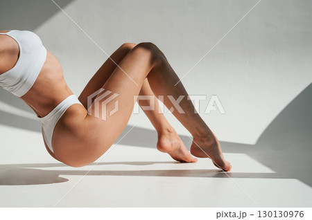 Shadows and sunlight. Doing exercises. Woman in white underwear with slim body type Shadows and sunlight. Doing exercises. Woman in white underwear with slim body type 130130976