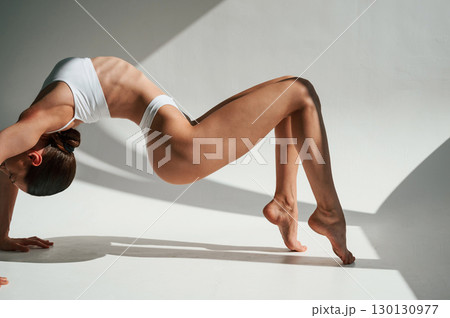 Shadows and sunlight. Doing exercises. Woman in white underwear with slim body type 130130977