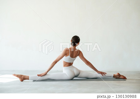 Stretching the legs. Fitness woman is indoors in white clothes Stretching the legs. Fitness woman is indoors in white clothes 130130988