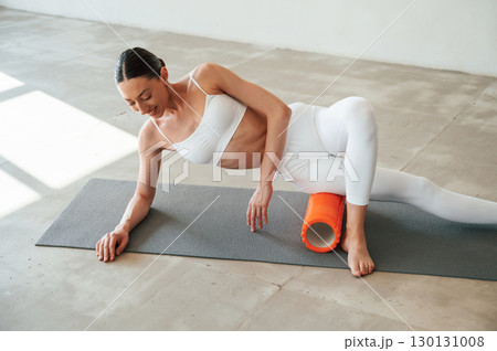 Roller for exercises. Fitness woman is indoors in white clothes Roller for exercises. Fitness woman is indoors in white clothes 130131008