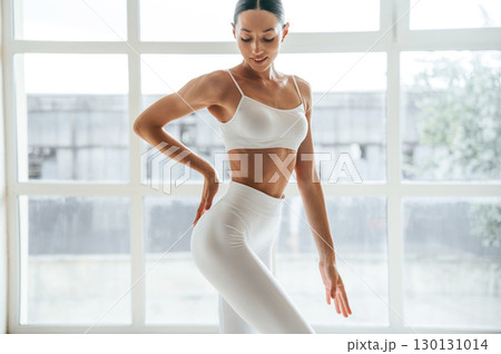 Natural lighting. Woman in fitness clothes is standing against window with view 130131014