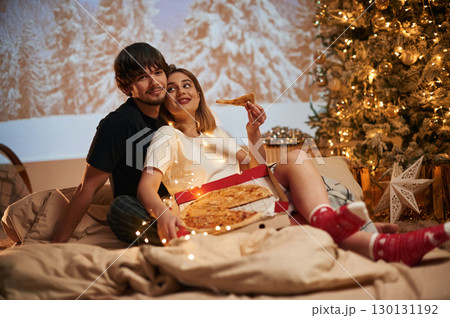Delicious pizza. Beautiful young couple indoors, celebrating new year against projector 130131192