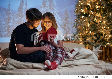 Woman is opening gift. Beautiful young couple indoors, celebrating new year against projector 130131205