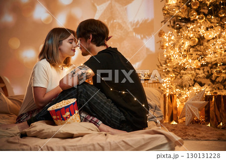 Cozy room with fir tree. Beautiful young couple indoors, celebrating new year against projector Cozy room with fir tree. Beautiful young couple indoors, celebrating new year against projector 130131228