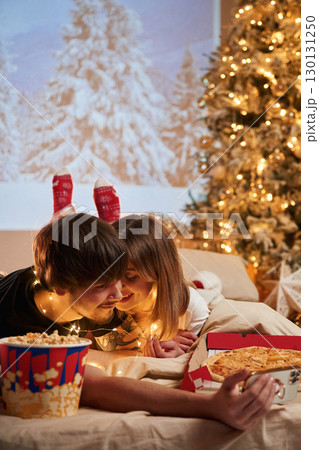 Taking photo by phone. Beautiful young couple indoors, celebrating new year against projector 130131250