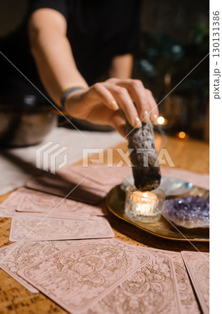 Practicing tarot card reading with crystals and incense in a cozy indoor setting during evening hours Practicing tarot card reading with crystals and incense in a cozy indoor setting during evening hours 130131386
