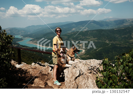 Woman with two dogs posing on rocks, enjoying stunning panoramic view of Stara Planina mountains and turquoise river. Travel and hiking with pets concept. 130132547