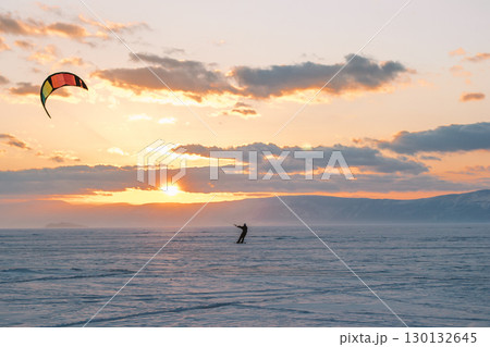kite surfer maneuvers skillfully across vast winter landscape under vibrant sunset sky. 130132645