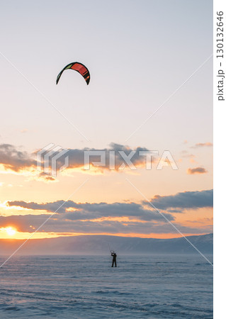 kite flyers enjoy breathtaking sunset while practicing their sport on frozen landscape in winter. 130132646