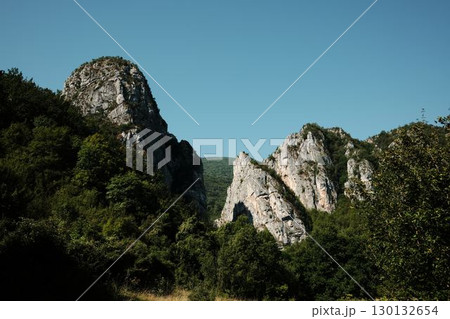 Majestic rocky peaks rising above dense green forest under a clear blue sky in Stara Planina, Serbia Majestic rocky peaks rising above dense green forest under a clear blue sky in Stara Planina, Serbia 130132654