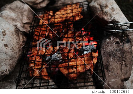 Close-up of grilled chicken on a stone campfire, cooking outdoors in nature. Rustic camping food preparation 130132655