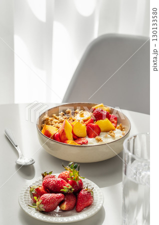 Granola or muesli with natural greek yogurt, strawberry and peach in a bowl on a white table Granola or muesli with natural greek yogurt, strawberry and peach in a bowl on a white table 130133580