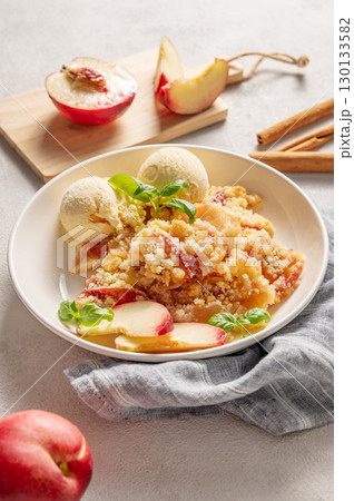 Peach crumble or cobbler with vanilla ice cream scoops and cinnamon on a plate on a light background 130133582