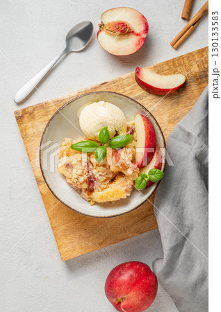 Peach crumble or cobbler with vanilla ice cream scoops and cinnamon in a plate on a wooden board 130133583