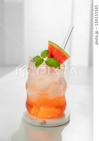 Watermelon mojito cocktail with ice and mint in a glass on a marble stand on a white table Watermelon mojito cocktail with ice and mint in a glass on a marble stand on a white table 130133585