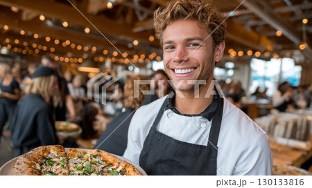 Friendly chef holding delicious freshly baked pizza in cozy restaurant interior 130133816