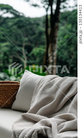 Elegant couch featuring a soft blanket and pillow, perfectly set in a tranquil outdoor space surrounded by lush greenery 130134413