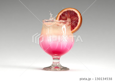 Vibrant cocktail splashes in a glass with a blood orange slice, showcasing creative mixology on a bright white surface 130134538
