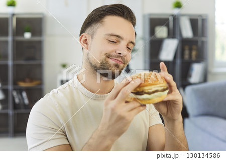 Young man enjoying delicious burger at home, close-up Young man enjoying delicious burger at home, close-up 130134586