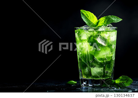 Vibrant cocktail made with fresh ingredients, ice, and mint leaves presented elegantly in a glass on a black backdrop 130134637