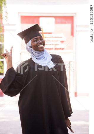 Portrait of happy african woman wearing hijab and graduation gown.  130135097