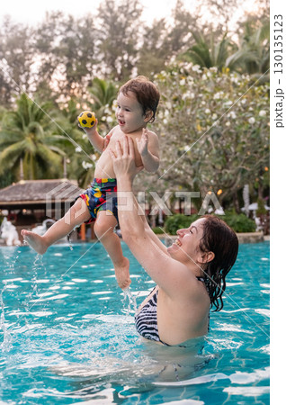 Caucasian woman holds her son while swimming in a pool on vacation. Mom teaches little boy to swim.  130135123