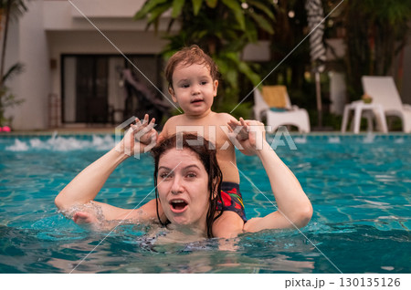 Caucasian woman holds her son while swimming in a pool on vacation. Mom teaches little boy to swim. Caucasian woman holds her son while swimming in a pool on vacation. Mom teaches little boy to swim. 130135126