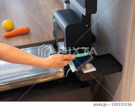 A woman pays using her smartphone at a self-checkout.  130135216