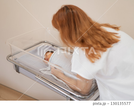 A young mother admires her newborn son in the maternity hospital. A young mother admires her newborn son in the maternity hospital. 130135577
