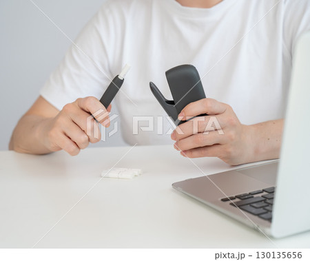 A woman takes a tobacco heating system out of a charger. Electronic cigarette. A woman takes a tobacco heating system out of a charger. Electronic cigarette. 130135656
