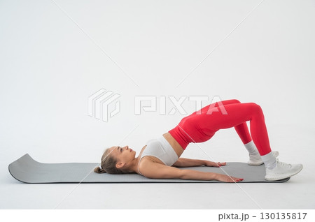 Young woman doing glute bridge on white background. 130135817