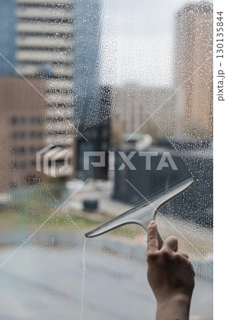 A woman washes a window with a scraper. A woman washes a window with a scraper. 130135844