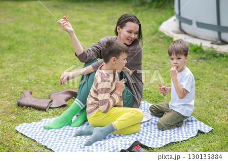 Caucasian woman eats fried sausages with her sons at a picnic. Caucasian woman eats fried sausages with her sons at a picnic. 130135884