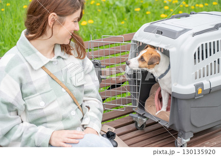 Caucasian woman traveling with dog. Owner sits on bench with Jack Russell Terrier in cage for safe travel. 130135920