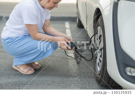 A woman pumps up a tire on a car.  130135935