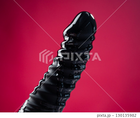 Lube pouring on black dildo on pink background.  130135982