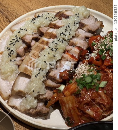 Tender slices of bossam, Korean boiled pork belly, served with fresh lettuce, garlic, and ssamjang. This flavorful and savory dish is perfect for wrapping and sharing in a traditional Korean meal. 130136525