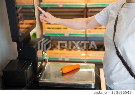 A woman weighs carrots at a self-checkout.  130136542