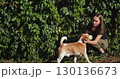 Young veterinarian crouching near a vibrant green leaves wall, gently examining a beagle dog on a sunny day, lovingly touching the dog's head with care and attention 130136673
