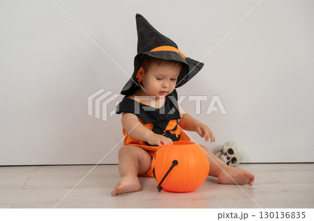 Cute caucasian boy in halloween pumpkin costume holding candy basket on white background.  130136835