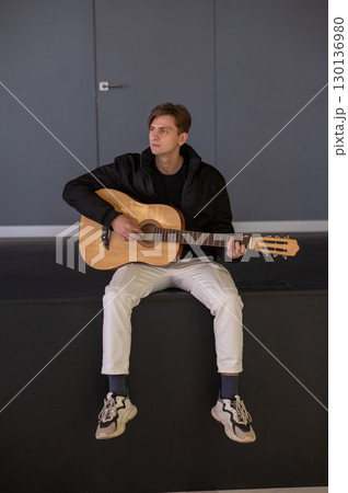 Caucasian man playing guitar while sitting on stage.  130136980